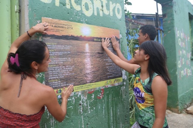 Manoela, Carol e Pablo colam um minidoor fora do barracão para completar a divulgação do festival dentro da comunidade Cabelo Seco.